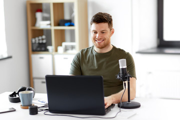 technology, mass media and podcast concept - happy young male audio blogger with laptop computer and microphone broadcasting at home office