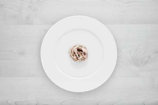 Small portion of tagliatelle pasta on round white plate on a white wooden table. Concept of dieting, healthy and less eating.