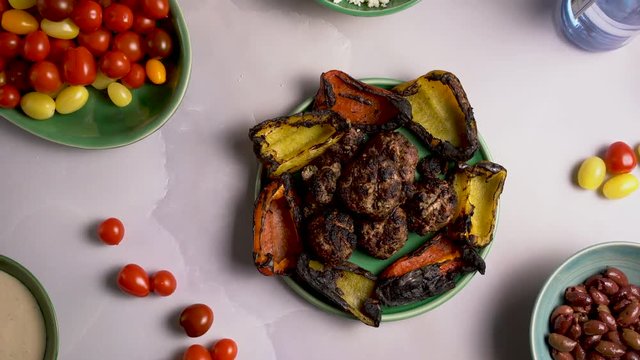 Closeup flat lay of kofta, roasted peppers, tomatoes, and ouzo and raki with olives, feta cheese and tzatziki.