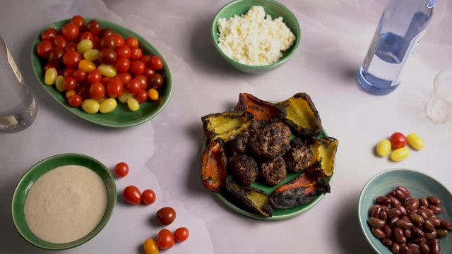 Flat lay of kofta, roasted peppers, tomatoes, and ouzo and raki with olives, feta cheese and tzatziki.