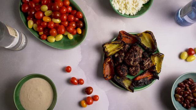 Flat lay of kofta, roasted peppers, tomatoes, and ouzo and raki with olives, feta cheese and tzatziki.