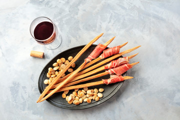 Italian antipasti. Grissini with a glass of red wine, parma ham and roasted almonds, shot from the top on a grey concrete background with a place for text