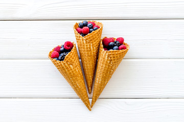 Summer breakfast with fresh berries in waffle cones on white wooden background top view
