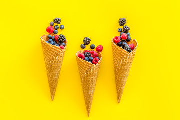 Fresh berries in waffle cones on yellow background top view