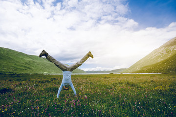 Woman hiker doing a handstand on high altitude mountain meadow