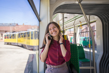 Young woman passenger standing with  smartphone while moving in the modern tram, enjoying trip at the public transport