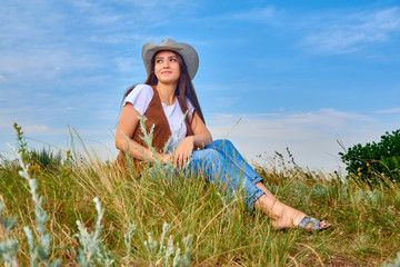 Girl in cowboy dress standing back on the top of Caucasus mountain with a scenery view to sunset at green valley. Female travel nature concept.