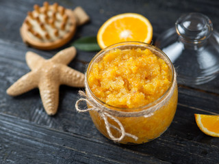 Orange scrub in a glass jar on a wooden table with orange slices and a starfish