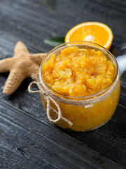 Orange scrub in a glass jar on a wooden table with orange slices and a starfish