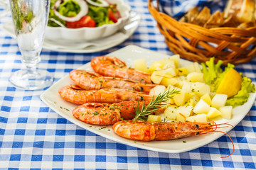 Large grilled shrimps with boiled potatoes on a white plate in a restaurant on the table.