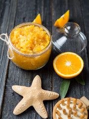 Orange scrub in a glass jar on a wooden table with orange slices and a starfish