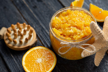 Orange scrub in a glass jar on a wooden table with orange slices and a starfish