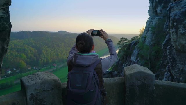 Female tourist with backpack taking pictures of beautiful view in the mountains, Saxon Switzerland 