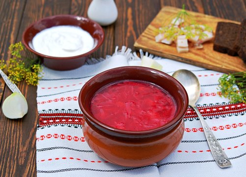 Borscht, hot soup with beets, cabbage and carrots in a clay bowl. Served with sour cream, rye bread and bacon.