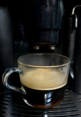 transparent large mug of freshly brewed coffee beans in a large black coffee machine