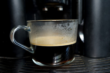 transparent large mug of freshly brewed coffee beans in a large black coffee machine