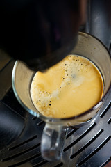 transparent large mug of freshly brewed coffee beans in a large black coffee machine