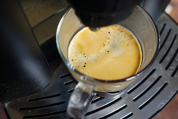transparent large mug of freshly brewed coffee beans in a large black coffee machine