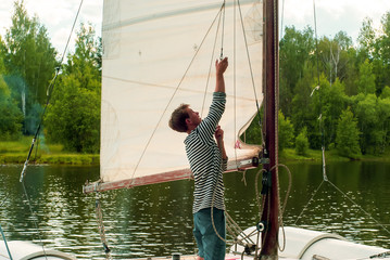 young sailor raises sail on a small sailing catamaran