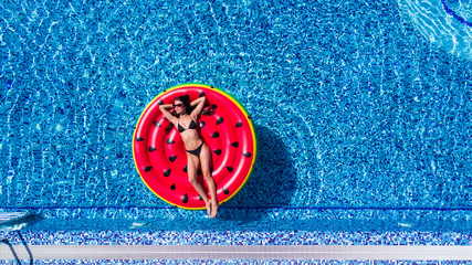 Beautiful young woman in bikini with inflatable watermelon tanning in pool. Above view of Woman in...