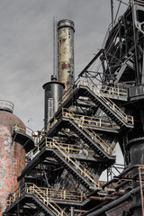 Exterior details of industrial manufacturing facility, smoke stacks and metal stairs, vertical aspect