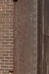 Riveted steel corner with heavy rust patina, brown brick, copy space, vertical aspect