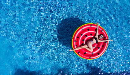 Top view of young woman relaxing on watermelon in pool. Young girl floating with fruit mattress....