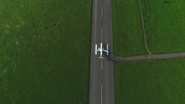 Aerial view of chasing aircraft, which takes off the runaway in the middle of green lawn. 4K.