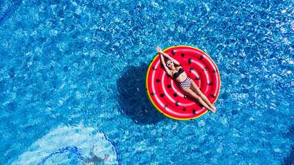 Young pretty woman relaxing on watermelon in pool floating with fruit mattress.