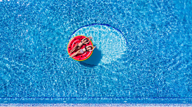 Aerial view of young pretty woman lying on inflatable watermelon mattrass floating and relaxing in swimming pool. Summer vocation.