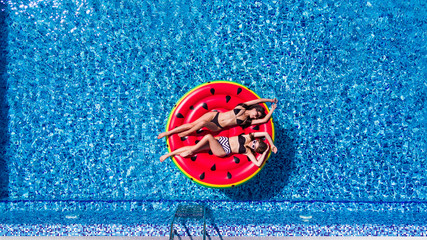 Aerial view of young pretty woman lying on inflatable watermelon mattrass floating and relaxing in swimming pool. Summer vocation.
