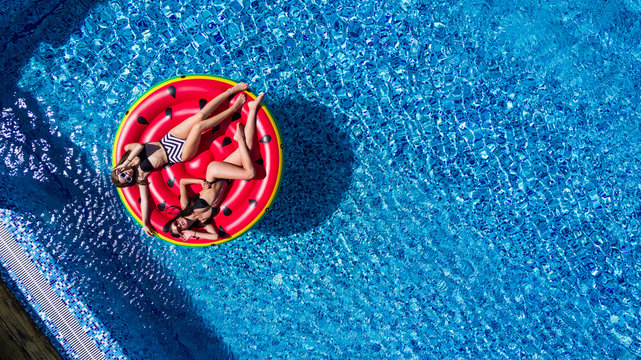 Aerial view of young pretty woman lying on inflatable watermelon mattrass floating and relaxing in swimming pool. Summer vocation.