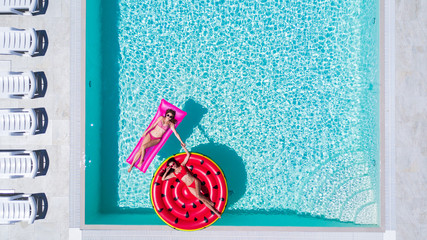 Aerial view of two women floating on inflatable mattresses relaxing in the swimming pool. Summer...