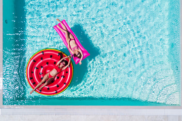 Aerial view of two women floating on inflatable mattresses relaxing in the swimming pool. Summer...