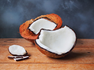 Coconut in half and coconut piece on wooden table with a grey background.
