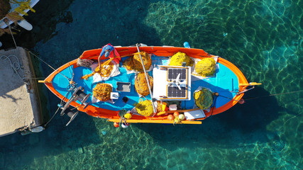 Aerial drone top view photo of traditional colourful fishing boat near iconic beach of Ornos with emerald clear sea, Mykonos island, Cyclades, Greece