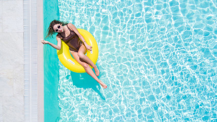 Happy young woman in bikini with rubber inflatable float, playing and having a good time at water fun park pool, on a summer hot day