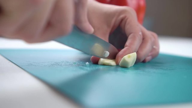 Female hands cutting garlic on a cutting board with red pepper on the background