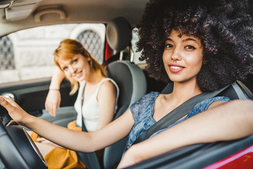 Two young women friends driving in the city - Millennials use the car to get around - People look...