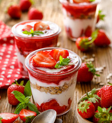 Strawberry layered dessert, healthy dessert with fresh strawberries, natural yoghurt, strawberry mousse and granola in glass dishes on a wooden table. Delicious and nutritious dessert or breakfast