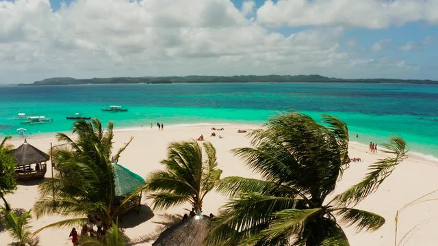 Sandy beach with tourists, palm trees and turquoise water on the island of Daco, Philippines, aerial view. Summer and travel vacation concept
