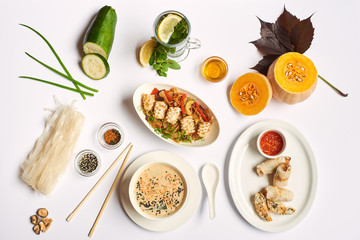 Flat lay of oriental dinner from soup with seeds, tempura shrimps and noodles with vegetables preparing for client. Three dishes lunch with mint tea ready for eating on white tablecloth.