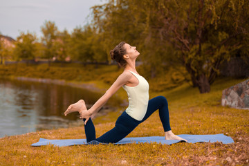 Slim brunette girl goes in for sports and performs yoga poses in the fall in nature by the lake