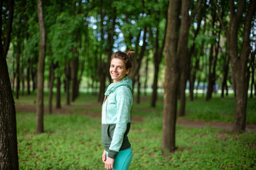 Fototapeta premium Thin brunette girl plays sports and performs beautiful and sophisticated yoga poses in a summer park. Green lush forest on the background. Woman doing exercises on a yoga mat