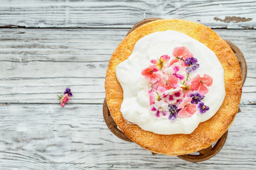 Victoria Sponge Cake with whipped cream and Sugared Flowers over a white wooden rustic table top. Image shot for above.