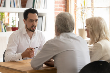 Confident bank manager consulting old senior couple clients at meeting