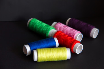 Bright colored threads for sewing on a dark background. Needlework concept and handmade. Sewing and repairing clothes