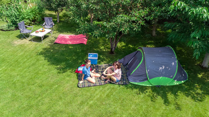 Aerial top view of campsite from above, mother and daughter having fun, tent and camping equipment...