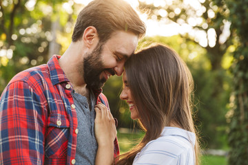 Fototapeta premium Image of young couple man and woman hugging and smiling while walking in green park