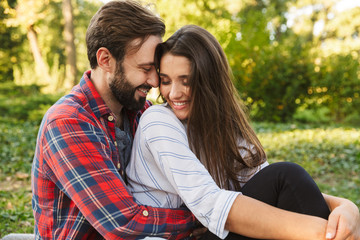 Image of happy couple man and woman hugging while resting in green park